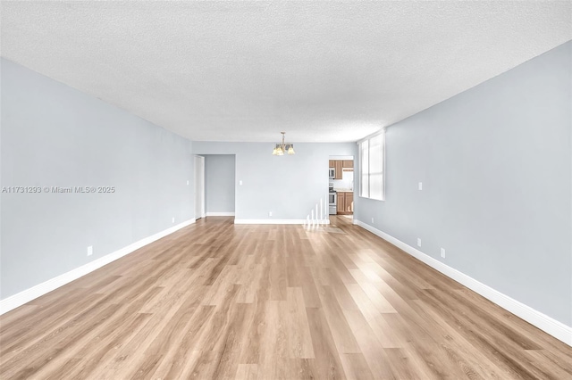 unfurnished living room featuring light hardwood / wood-style flooring, an inviting chandelier, and a textured ceiling