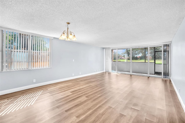 empty room with light wood-type flooring, a chandelier, and a textured ceiling