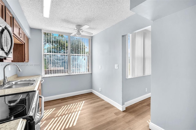 kitchen with light wood-type flooring, stainless steel appliances, sink, ceiling fan, and a textured ceiling