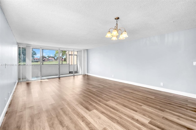 empty room with an inviting chandelier, a wall of windows, light hardwood / wood-style flooring, and a textured ceiling