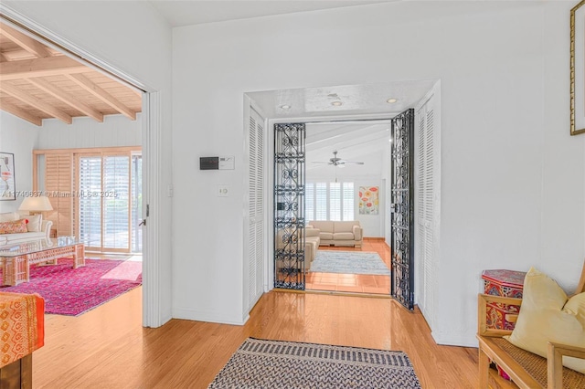 doorway with beamed ceiling, ceiling fan, and light hardwood / wood-style flooring