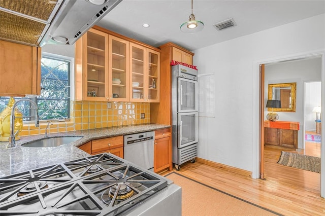 kitchen with appliances with stainless steel finishes, tasteful backsplash, sink, light stone counters, and light wood-type flooring