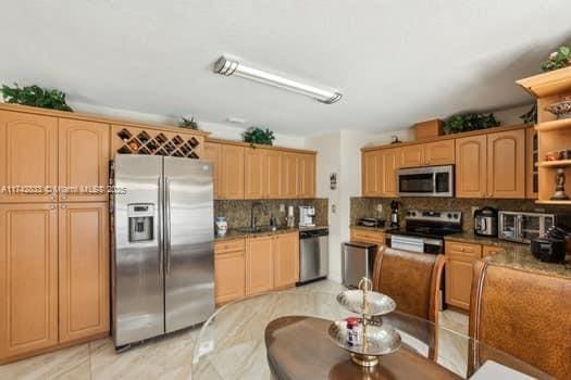 kitchen featuring sink, backsplash, stainless steel appliances, and dark stone counters