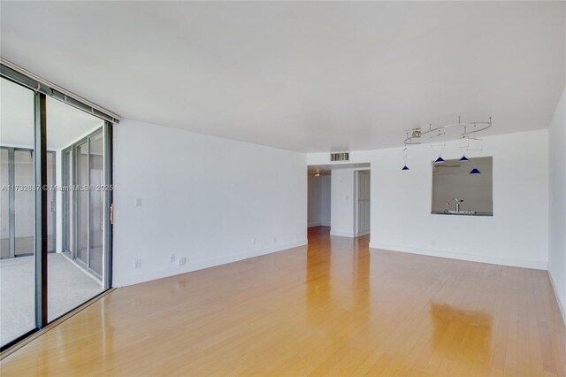 spare room with baseboards, visible vents, a wall of windows, and wood finished floors