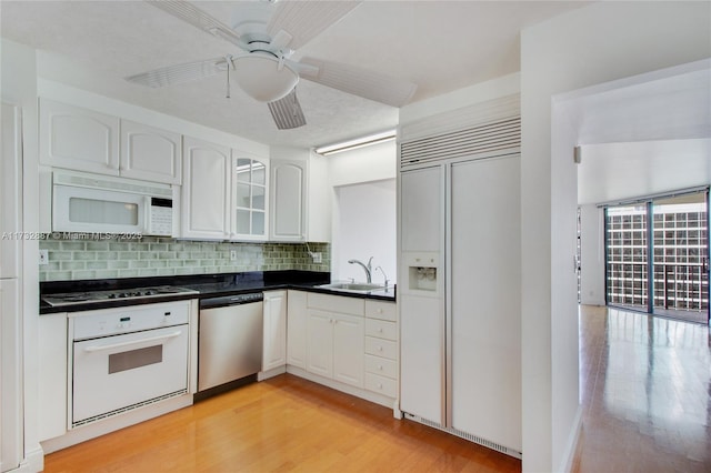 kitchen with white appliances, white cabinetry, light wood-style floors, backsplash, and dark countertops