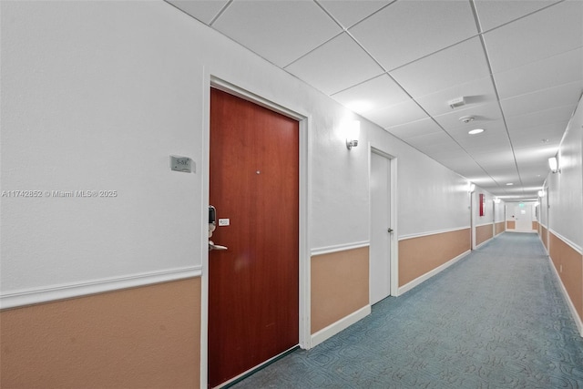 hall featuring a drop ceiling, carpet, and baseboards