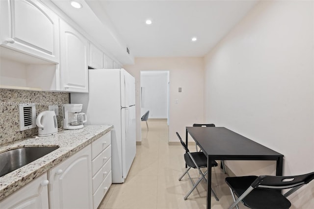 kitchen featuring light tile patterned floors, decorative backsplash, light stone counters, freestanding refrigerator, and white cabinetry