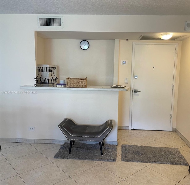 foyer entrance with visible vents, a textured ceiling, baseboards, and light tile patterned flooring