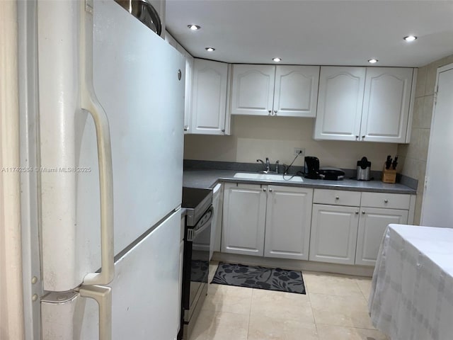 kitchen featuring range with electric cooktop, a sink, freestanding refrigerator, and white cabinetry