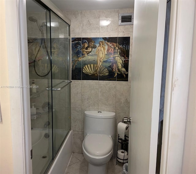 bathroom featuring tile patterned flooring, toilet, bath / shower combo with glass door, visible vents, and tile walls