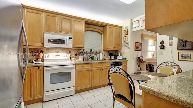 kitchen featuring light stone counters, light tile patterned floors, tasteful backsplash, a sink, and white appliances