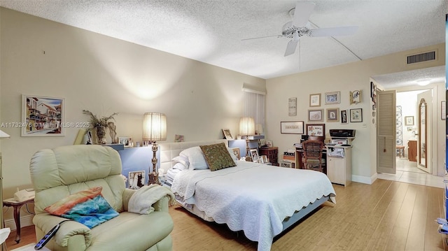 bedroom with a textured ceiling, ceiling fan, visible vents, baseboards, and light wood-style floors