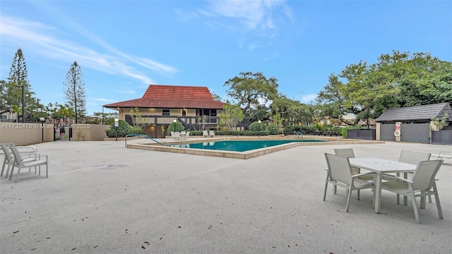 community pool with a patio area, fence, and an outdoor structure