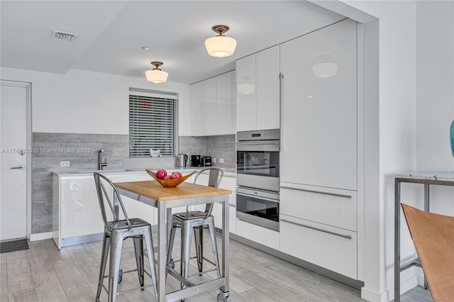 kitchen with stainless steel double oven, sink, light hardwood / wood-style floors, and white cabinets