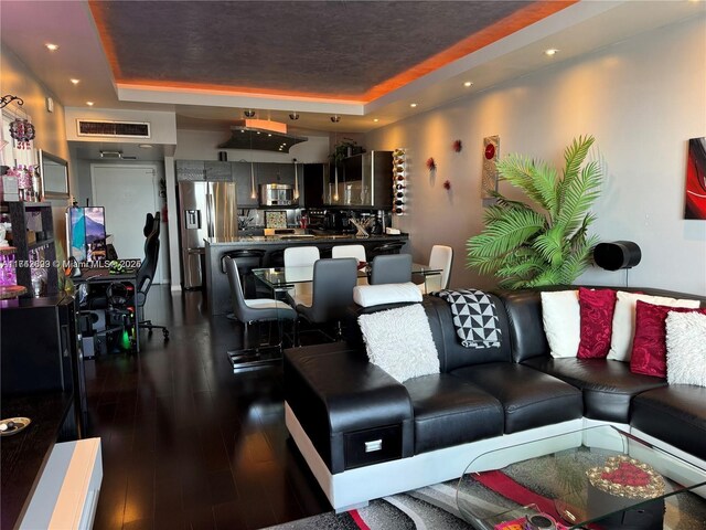living room featuring a raised ceiling and dark hardwood / wood-style flooring