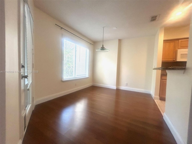 unfurnished dining area featuring dark wood-style floors, visible vents, and baseboards