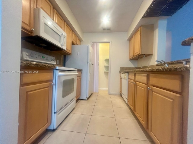 kitchen featuring light tile patterned floors, visible vents, dark stone counters, white appliances, and baseboards