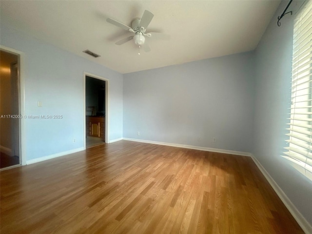 empty room featuring a wealth of natural light, visible vents, ceiling fan, and wood finished floors