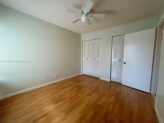 unfurnished bedroom with multiple closets, a ceiling fan, baseboards, and wood finished floors