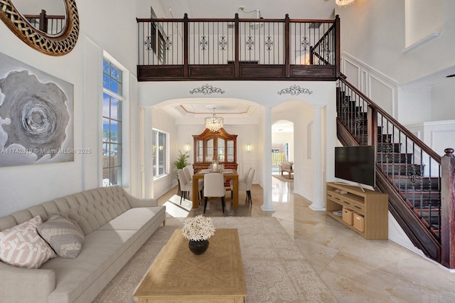 living room with ornate columns, a towering ceiling, a wealth of natural light, and an inviting chandelier