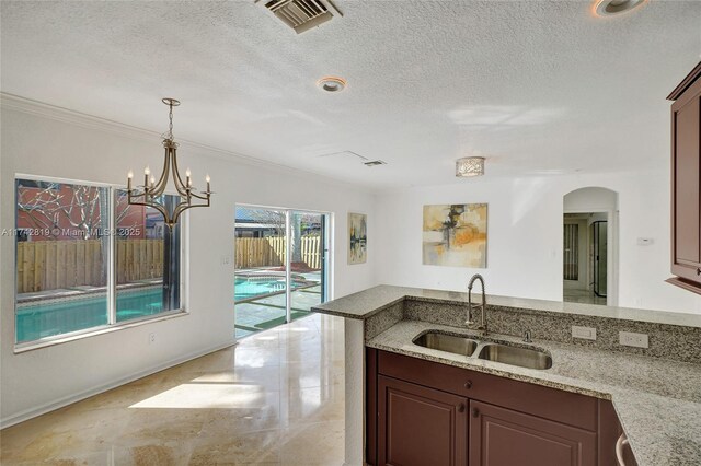 kitchen with sink, a chandelier, a textured ceiling, ornamental molding, and light stone countertops