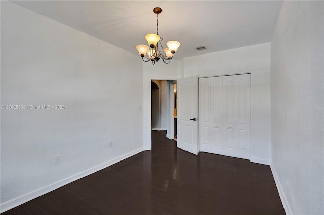 unfurnished bedroom featuring dark wood-type flooring, a chandelier, and a closet