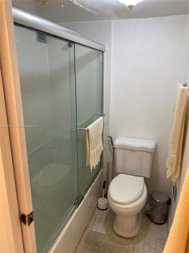 bathroom featuring tile patterned flooring, combined bath / shower with glass door, and toilet