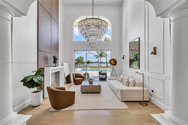 living room featuring a notable chandelier, a towering ceiling, light hardwood / wood-style floors, and ornate columns