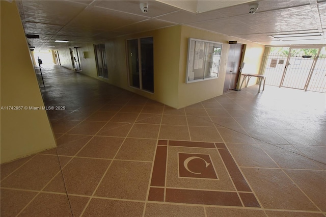 corridor featuring tile patterned flooring, a healthy amount of sunlight, and a paneled ceiling