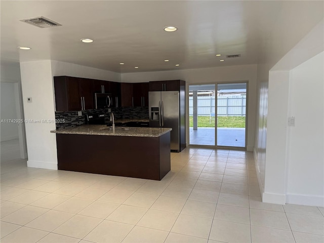 kitchen featuring light tile patterned flooring, dark brown cabinetry, tasteful backsplash, dark stone countertops, and stainless steel appliances