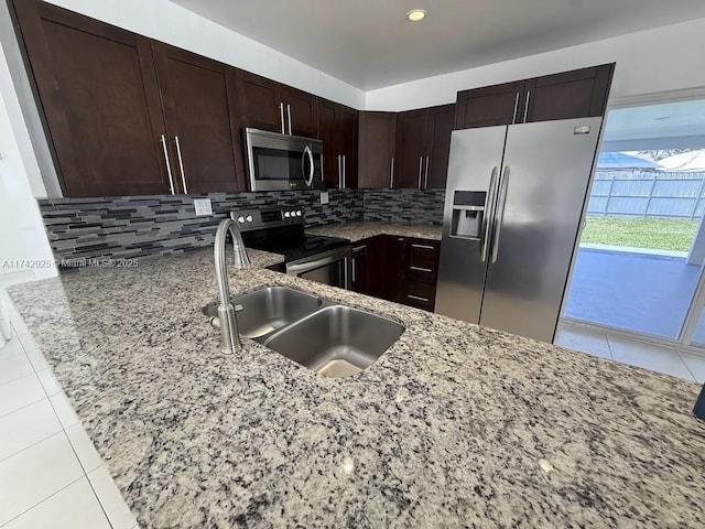 kitchen with light tile patterned floors, sink, appliances with stainless steel finishes, light stone counters, and tasteful backsplash