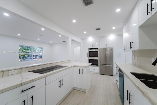 kitchen featuring sink, light stone counters, white cabinetry, stainless steel appliances, and light hardwood / wood-style floors