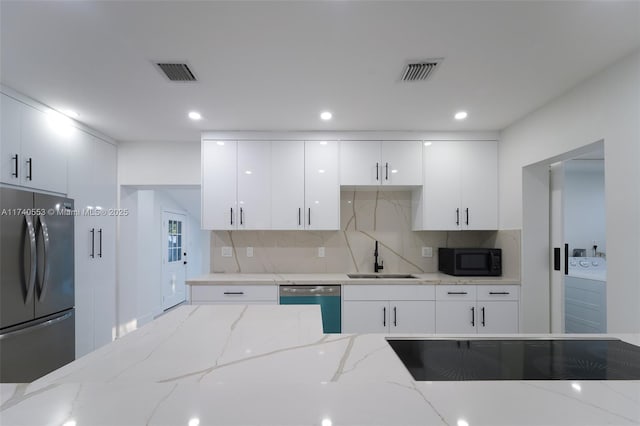 kitchen with sink, white cabinetry, appliances with stainless steel finishes, light stone countertops, and decorative backsplash