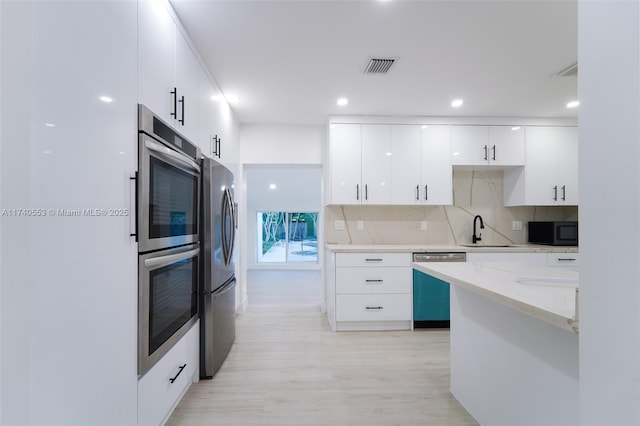 kitchen featuring sink, light hardwood / wood-style flooring, appliances with stainless steel finishes, backsplash, and white cabinets