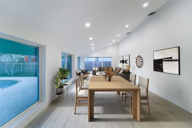 dining room with high vaulted ceiling and light hardwood / wood-style floors