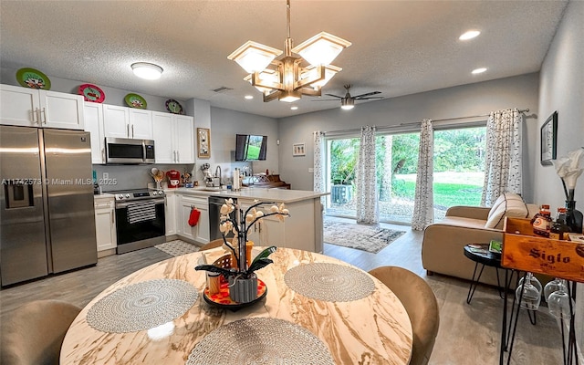 kitchen with sink, a textured ceiling, pendant lighting, stainless steel appliances, and white cabinets