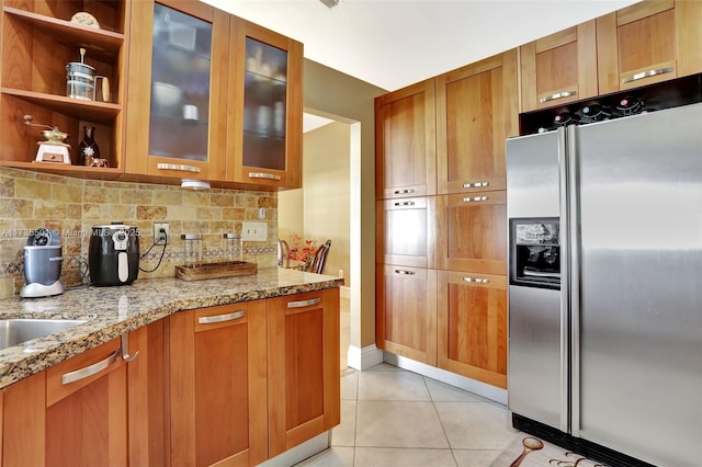 kitchen featuring stainless steel refrigerator with ice dispenser, light stone countertops, light tile patterned flooring, and backsplash