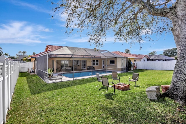 rear view of house with a fenced in pool, a yard, glass enclosure, and a fire pit