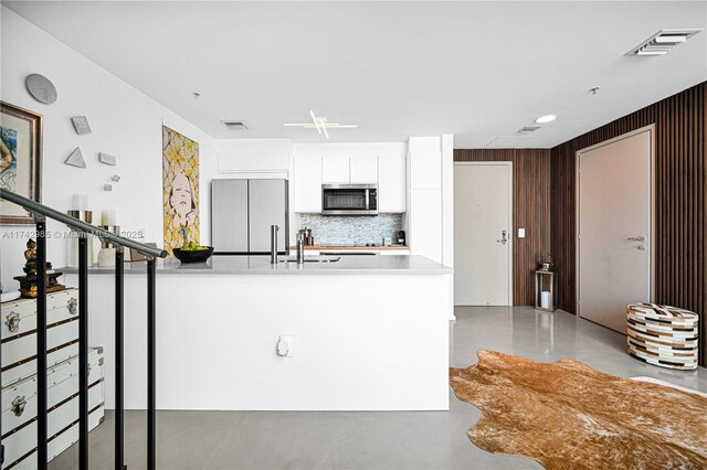 kitchen with refrigerator, backsplash, white cabinetry, concrete flooring, and wooden walls