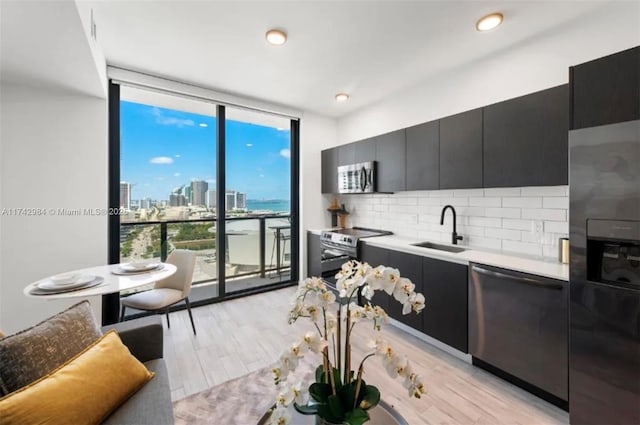 kitchen featuring sink, a wall of windows, decorative backsplash, stainless steel appliances, and light wood-type flooring