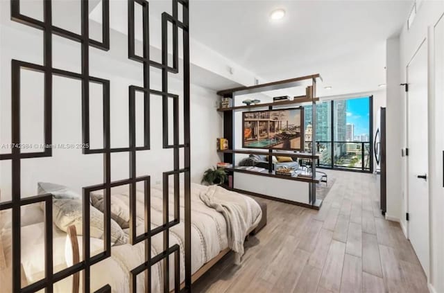 bedroom with expansive windows, hardwood / wood-style floors, and stainless steel refrigerator