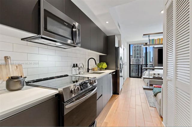 kitchen featuring sink, light wood-type flooring, expansive windows, stainless steel appliances, and decorative backsplash