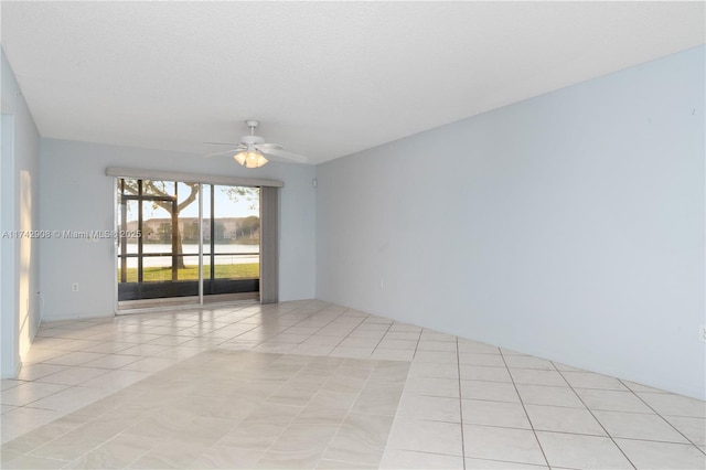 empty room featuring light tile patterned flooring, a water view, a textured ceiling, and ceiling fan