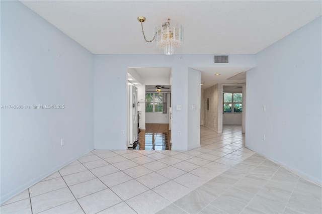 empty room with ceiling fan with notable chandelier and light tile patterned floors