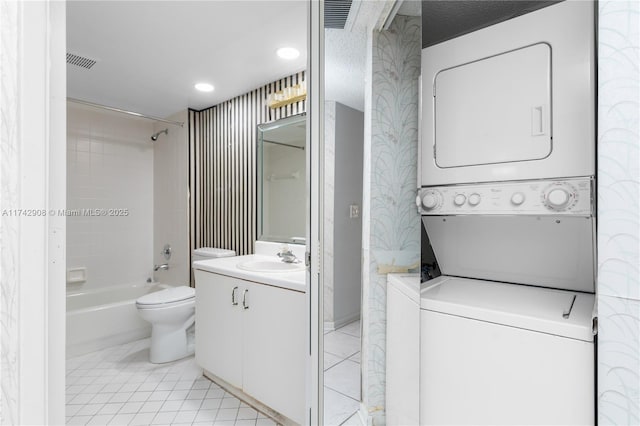 interior space featuring tiled shower / bath, vanity, stacked washer / drying machine, toilet, and tile patterned floors