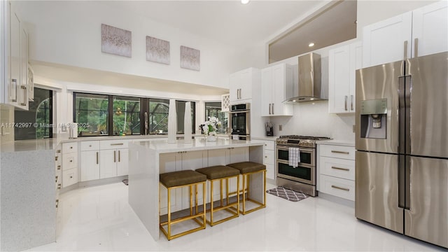 kitchen featuring white cabinets, appliances with stainless steel finishes, a center island, and wall chimney range hood