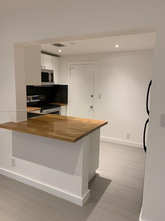 kitchen with appliances with stainless steel finishes, tasteful backsplash, white cabinetry, wooden counters, and kitchen peninsula