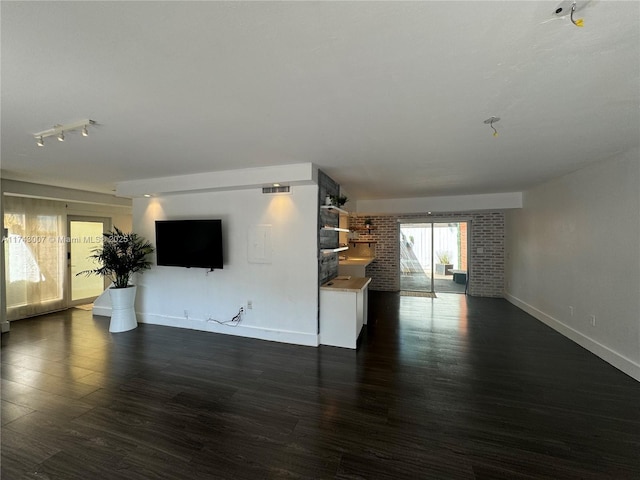 unfurnished living room with dark wood-type flooring and brick wall