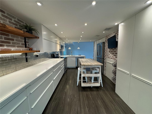 kitchen featuring stainless steel electric range, dark hardwood / wood-style floors, white cabinets, and brick wall