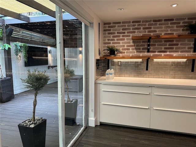 bar with white cabinetry, brick wall, and dark hardwood / wood-style floors